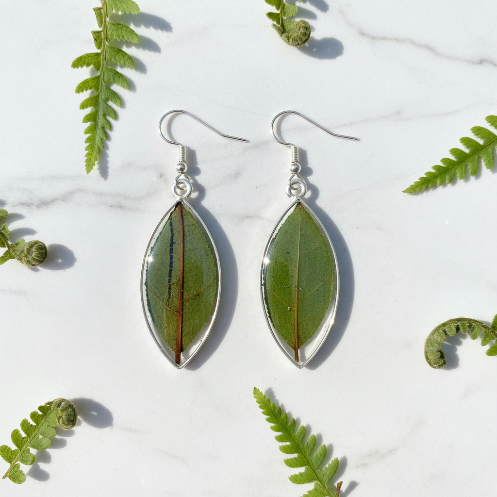 Natural leaf in resin teardrop earrings shown as a pair flat lay on white marble with small fern fronds