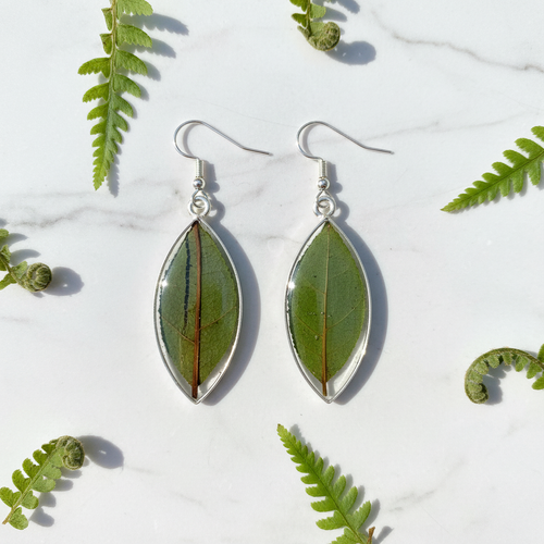 Natural leaf in resin teardrop earrings shown as a pair flat lay on white marble with small fern fronds