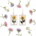 Pressed yellow flower rectangle dangle earrings flat lay on white surface with scattered dried wildflowers