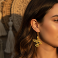 Tumbaga gold bird drop earrings with intricate cutout design worn on a model's ear