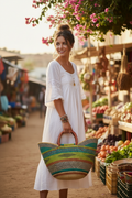 Woman in boho-chic outfit carrying oversized colorful Bolga tote at an outdoor café or market, bag prominently sized to show its generous 18-inch dimensions
