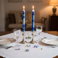 Hand-painted South African Feruzi design taper candles in cobalt and sky blue with African geometric symbols lit in silver holders on an elegant blue and white table